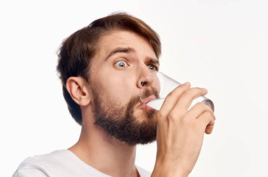 Yakışıklı adam bardaktan su içiyor. Şaşırmış görünüyor. Duyguları beyaz arka plan.