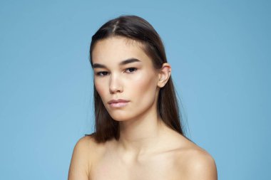 Esmer, çıplak omuzlu, kozmetik cilt bakımlı, mavi arka planlı.