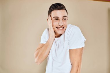 Duygusal adam beyaz tişörtlü, elleri yaşam tarzı bej arka planlı jestler