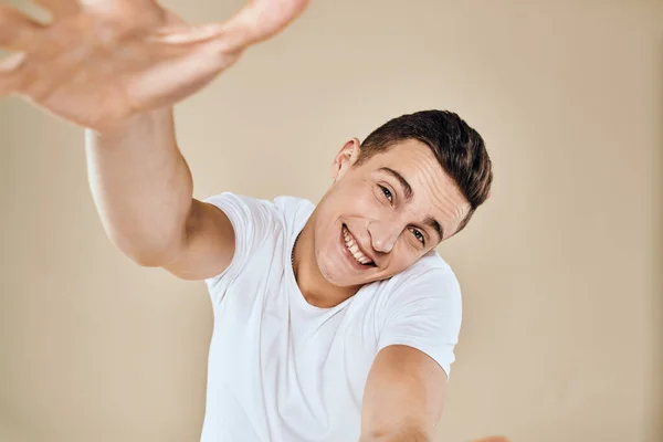 Симпатичный эмоциональный мужчина белая футболка жест с руками обрезанный вид бежевый студийный фон — стоковое фото