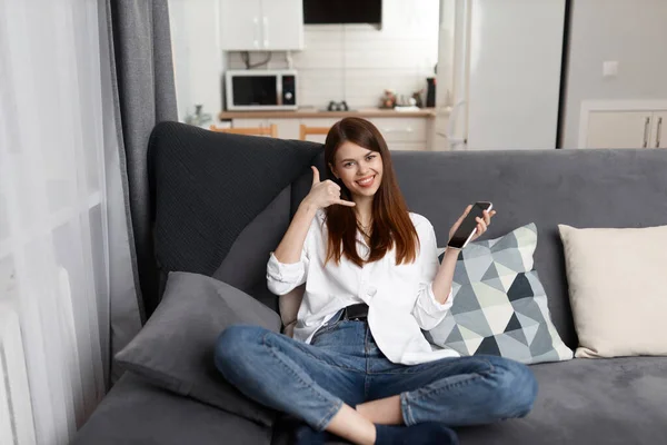 Mulher alegre falando ao telefone sentado no sofá descansando no apartamento — Fotografia de Stock