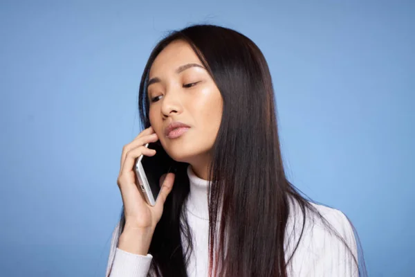 Азиатка разговаривает по мобильному телефону на синем фоне — стоковое фото