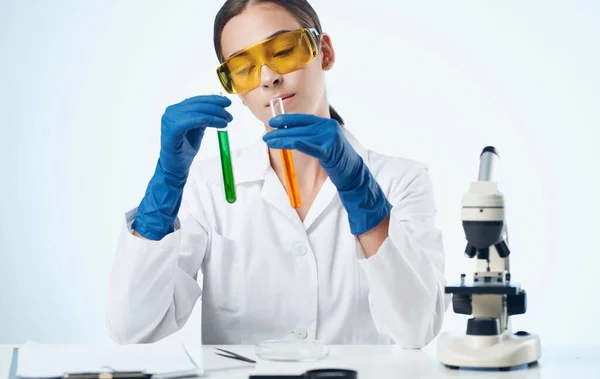 Жіночий лабораторний асистент в медичних рукавичках і колбі з рідким хімічним елементом мікроскопом — стокове фото