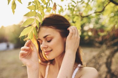 Kadın, yaprakların yakınındaki ağaçta çıplak omuzlu beyaz bir elbise giyiyor.
