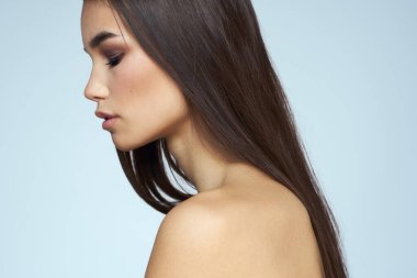 Güzel esmer, çıplak omuzlu, uzun saçlı, mavi arka planlı.