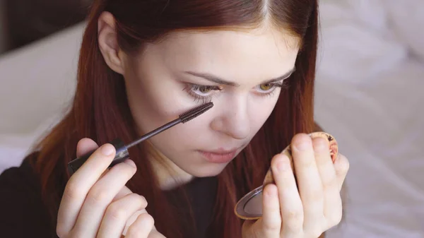 Frau malt Wimpern mit Spiegel in der Hand zur Selbstpflege Weiblichkeit — Stockfoto