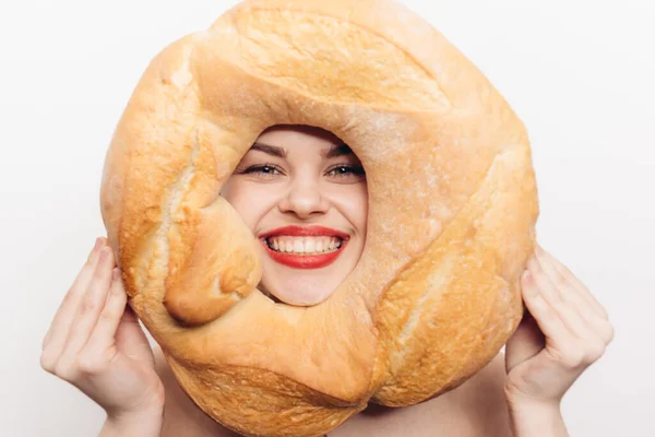 Happy woman with bright makeup holds a round loaf of bread in her hand and grimaces at the camera — Stock Photo, Image