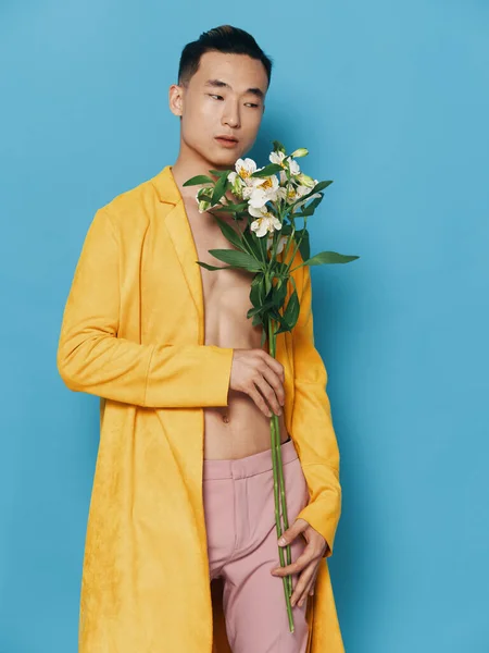 Aparência coreana masculina com um buquê de flores em um casaco amarelo e calças rosa — Fotografia de Stock