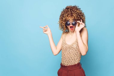 Güzel kadın, kıvırcık saçlı, elleri titrek, şaşırmış. 