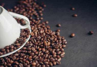 Tepside ters çevrilmiş beyaz fincan ve koyu arkaplanda serpiştirilmiş kahve çekirdekleri