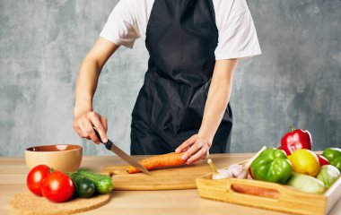 Siyah önlüklü bir kadın sebze doğruyor. Mutfakta taze yemek pişiriyor.