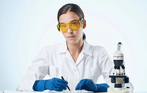 Assistente di laboratorio femminile in guanti medici e fiaschetta con microscopio ad elementi chimici liquidi — Foto Stock