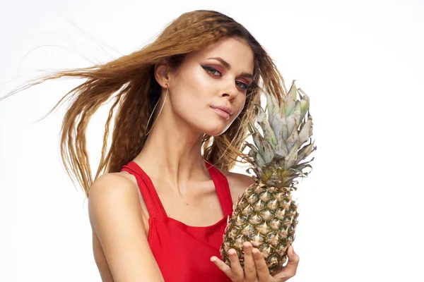Woman with ananas in hands faliste włosy czerwony t-shirt owoce lato wakacje lekkie tło — Zdjęcie stockowe