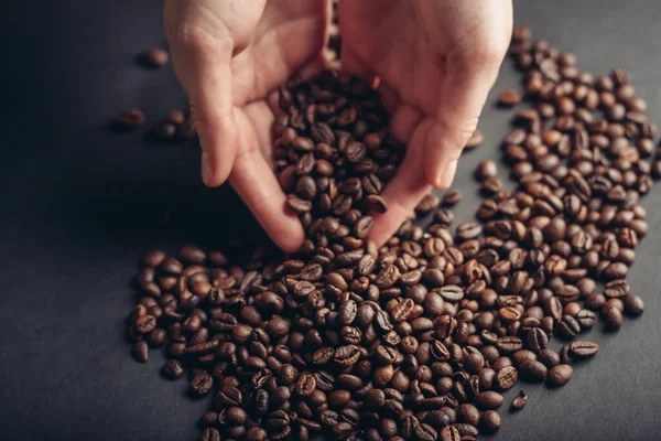Granos de café en manos esparcidas sobre un fondo oscuro — Foto de Stock