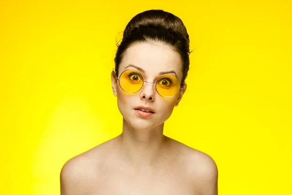 Esmer, çıplak omuzlu, sarı gözlüklü, duyguları kesik, manzaralı bir stüdyo. — Stok fotoğraf