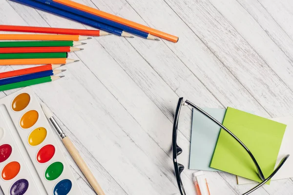 Írószer az irodai asztalon akvarell festékek poharak és színes ceruzák — Stock Fotó