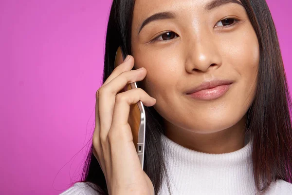 woman asian appearance talking on the phone cropped view studio pink background