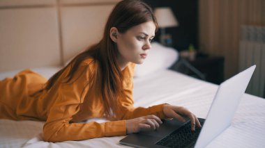 Kadın dizüstü bilgisayarın önünde yatağa uzanıyor. Serbest iş interneti.