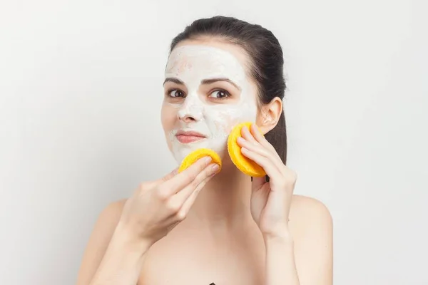 Femme joyeuse avec des épaules nues crème masque sur le visage gommage éponges dans les mains — Photo