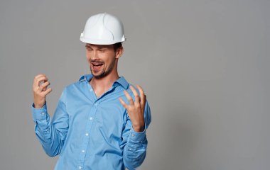 Beyaz kasklı ve mavi gömlekli bir mimar gri arka plan duygularının portresini yapıyor.