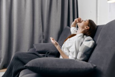 Mutlu kadın koltukta oturuyor, arkasında cep telefonu ve perdeler var.