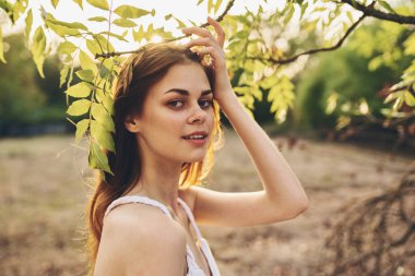 Doğadaki yeşil ağaçların yanında beyaz elbiseli romantik bir kadın.