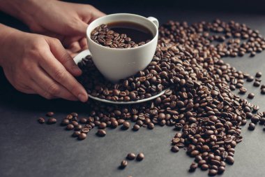 Gri bir masada aromatik kahve çekirdekleri ve bir bardağın yanında da bir bardak su.