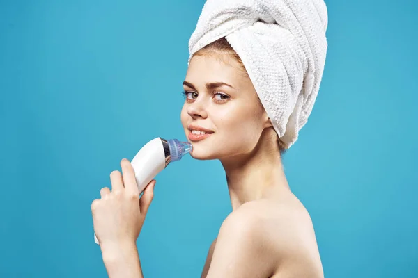 Mulher atraente com toalha na cabeça ombros nus massageador dermatologia cuidados da pele fundo azul — Fotografia de Stock