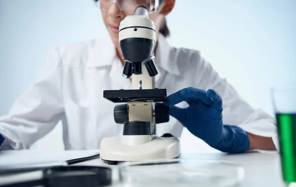 Assistante de laboratoire féminine examine les bactéries à travers un microscope et des lunettes sur la vaccination des éléments chimiques du visage — Photo