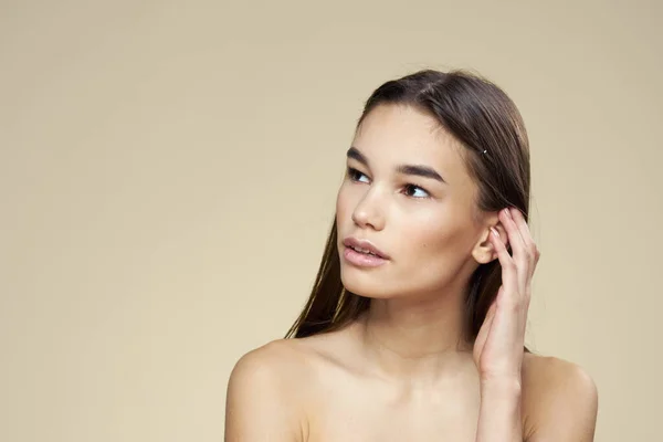 Mulher com ombros desnudados cabelo escuro maquiagem pele limpa fundo bege — Fotografia de Stock