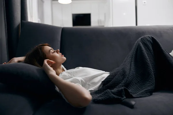 Mujer descansando acostada en un sofá bajo una manta gris —  Fotos de Stock