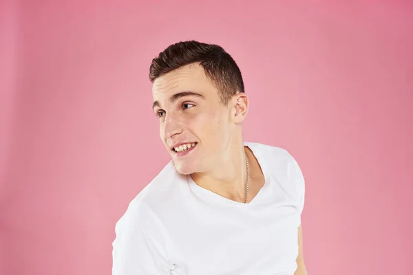 Un uomo in una t-shirt bianca gesti con le mani emozioni rosa sfondo studio ritagliato vista — Foto Stock