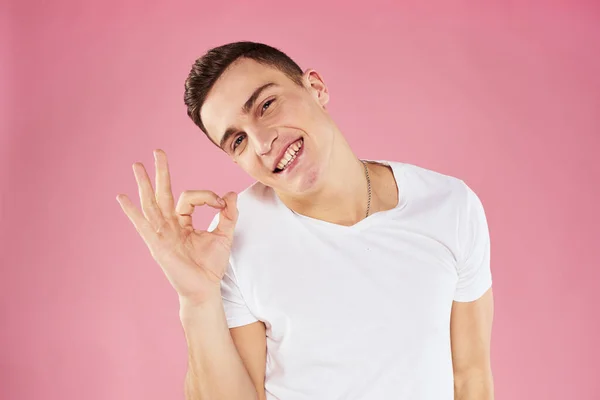 Ein Mann in einem weißen T-Shirt gestikuliert mit seinen Händen im rosafarbenen Hintergrund. — Stockfoto