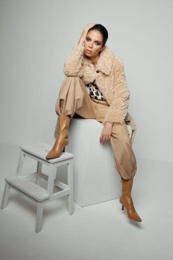 Güz çizmeli, bej ceketli kadın modellik yapıyor.