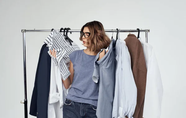 Känslomässig kvinna står nära kläder på en hängare i ett omklädningsrum på en ljus shopping bakgrund — Stockfoto