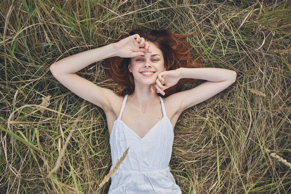 Mulher romântica em um vestido branco encontra-se em um palheiro na natureza e segura as mãos atrás de sua cabeça — Fotografia de Stock