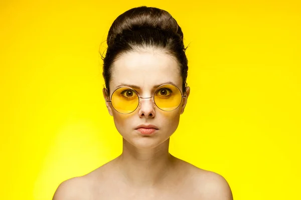 Çıplak omuzlu bir kadın. Sarı gözlükler. Yüzüne yakın eller. — Stok fotoğraf