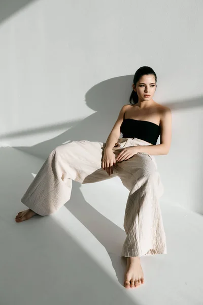 Mulher elegante vestindo roupas elegantes sentado encostado contra a parede dentro de casa — Fotografia de Stock
