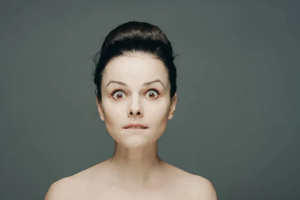 Porträt einer Frau mit nackten Schultern Emotionen gesammelt Haare in einem Dutt grauen Hintergrund — Stockfoto