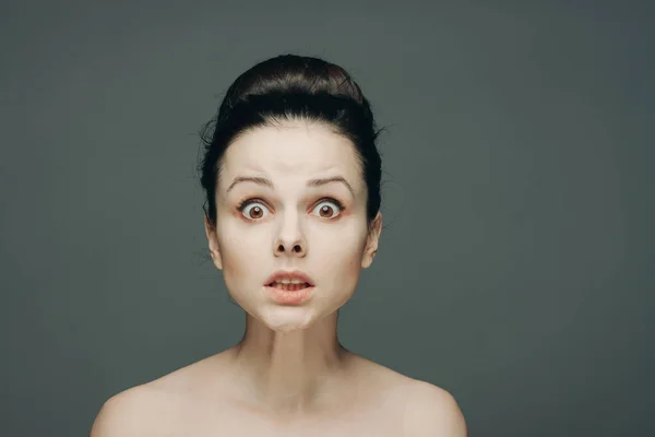 Porträt einer Frau mit nackten Schultern Emotionen gesammelt Haare in einem Dutt grauen Hintergrund — Stockfoto