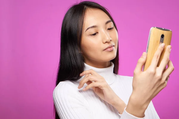 Hübsche Frau mit Telefon in den Händen weißer Pullover Technologie Kommunikation rosa Hintergrund — Stockfoto
