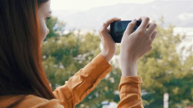 Elinde telefon olan kadın, kamera önünde doğanın resimlerini çekiyor.