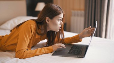 Kadın dizüstü bilgisayarla yatakta uzanıyor. Ev iletişim teknolojisinde çalışıyor.