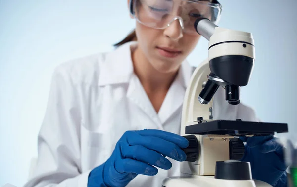 Asistente de laboratorio femenino examina las bacterias a través de un microscopio y gafas en la vacunación del elemento químico de la cara —  Fotos de Stock