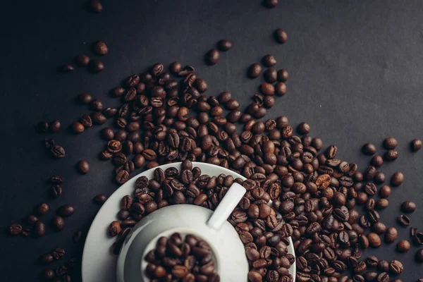 Taza blanca y platillo y granos de café grandes sobre un fondo oscuro macro fotografía — Foto de Stock