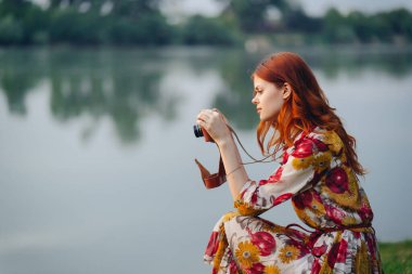 Nehir hobisinin yanında elinde kamera olan çok renkli elbiseli bir kadın.