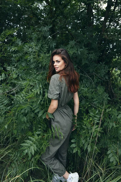 Woman In a trendy jumpsuit near green bushes and white sneakers outdoors green leaves