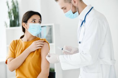 Tıbbi maskeli hasta elinde şırıngayla doktora bakıyor.