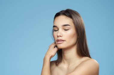 Esmer, çıplak omuzlu, kozmetik cilt bakımlı, mavi arka planlı.