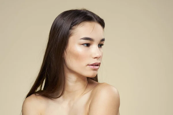 Mulher com ombros desnudados cabelo escuro maquiagem pele limpa fundo bege — Fotografia de Stock